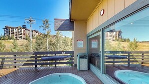 A spa area with two hot tubs, wooden deck, and a view of surrounding buildings.