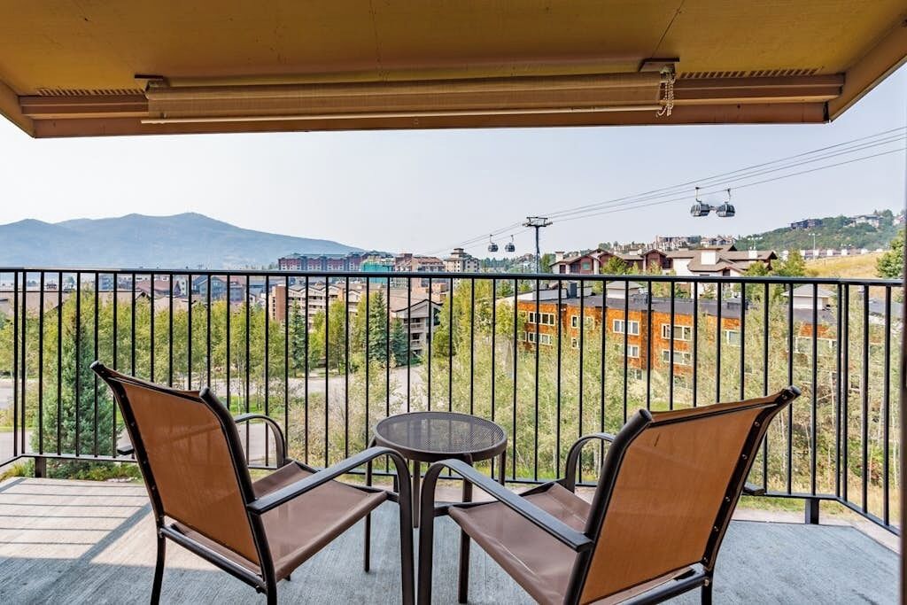 Un balcón con dos sillas y una mesa, con vista a un paisaje urbano que incluye edificios y una montaña al fondo.