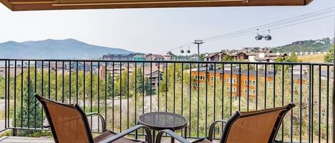 Un balcón con dos sillas y una mesa, con vista a un paisaje urbano que incluye edificios y una montaña al fondo.