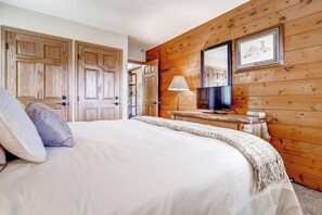 Ein Schlafzimmer mit einem Bett, Holzwänden, einem Nachttisch, einer Lampe und zwei Türen.