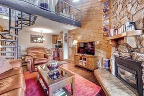 Ein geräumiger Wohnbereich mit Kamin, Fernseher und einer hohen Holzbalkendecke mit Balkon.