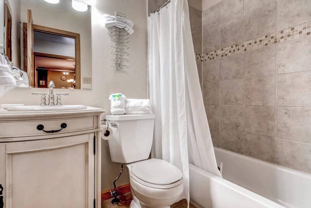 A bathroom with a toilet, sink, mirror, and shower curtain.