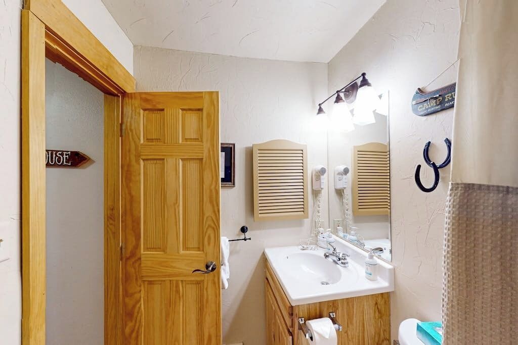 A bathroom with a wooden door, a sink, a mirror, and a towel rack.
