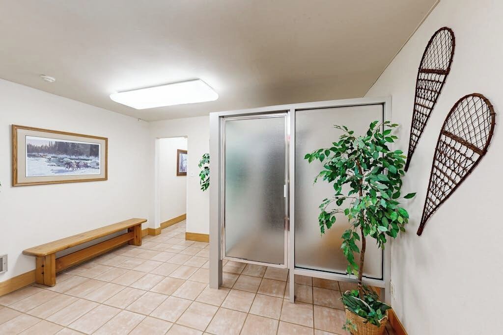 A hallway with a bench, a frosted glass partition, and a potted plant.