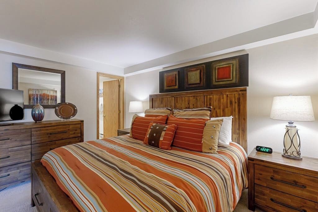 Ein Schlafzimmer mit Bett, Nachttischen, einem Schminktisch und einem Spiegel, sowie Bildern an der Wand.
