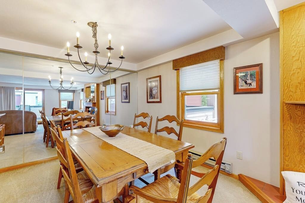 A dining area with a wooden table, chairs, a chandelier, and framed pictures on the walls.