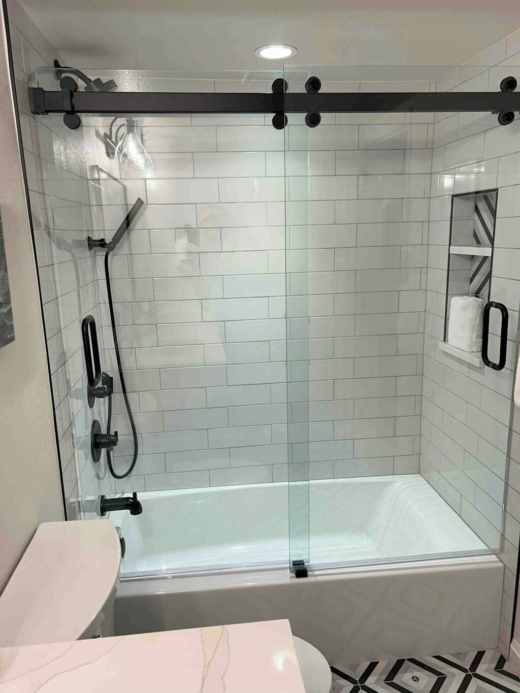 A modern bathroom with a glass-enclosed shower, a white bathtub, and a marble vanity.