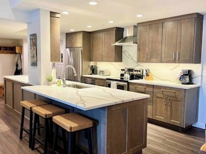 A modern kitchen with a central island, bar stools, stainless steel appliances, and wooden cabinetry. - Luxury remodel, ski in/out, top floor views + vaulted ceilings, pool/hot tubs (Steamboat Springs)
