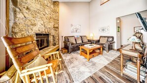 Ein gemütliches Wohnzimmer mit einer Steinwand, Ledersofa, Holzstühlen, einem Kamin und einem Bücherregal.