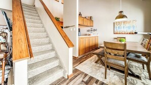 Eine Treppe führt zu einer Küchenzeile mit Holzausbau, einem Esstisch und einer Pendelleuchte.