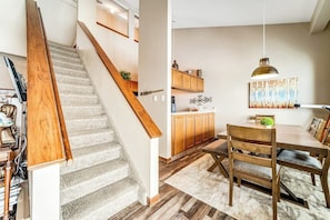 Eine Treppe führt zu einer Küchenzeile mit Holzausbau, einem Esstisch und einer Pendelleuchte.