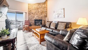 Ein Wohnzimmer mit Steinwand, Kamin, Ledersofa, Couchtisch aus Holz und Blick durch eine Glastür.