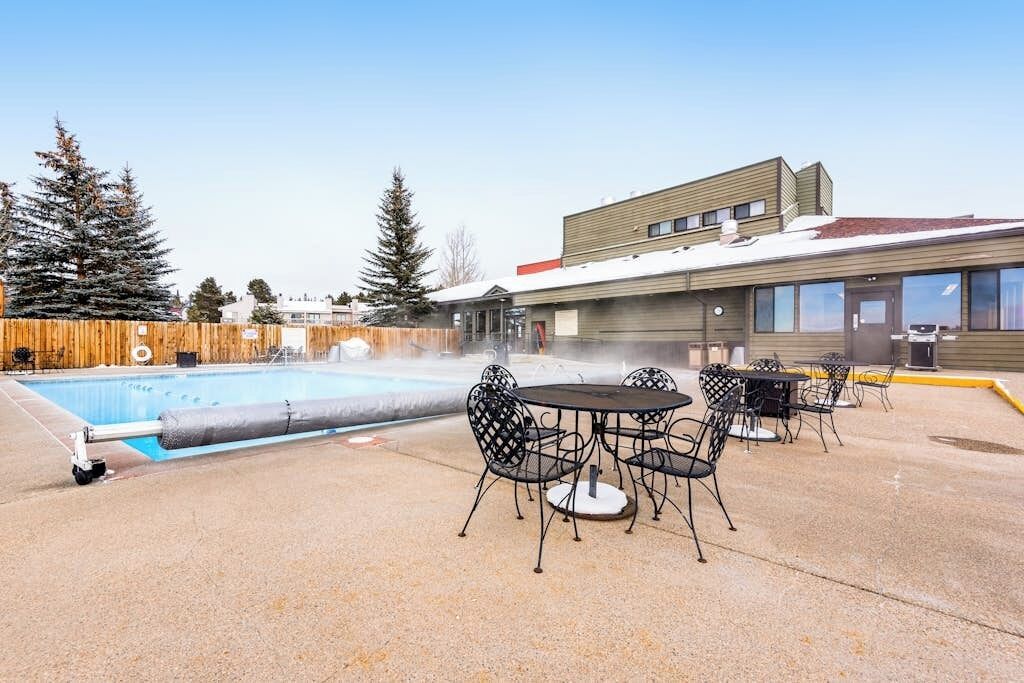 A pool with a hot tub, outdoor seating, and a building with multiple windows.