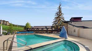 Uma piscina com área coberta, um espaço de estar coberto e vista para um edifício ao fundo.