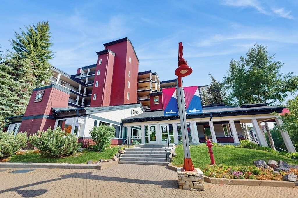 A multi-story hotel with a red facade, a covered entrance, and a red fire hydrant in the foreground.
