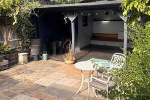 Un patio couvert avec une table et des chaises, une plante en pot et un tonneau.