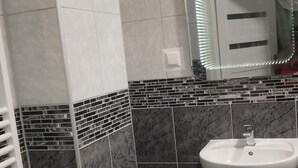 A bathroom with a white sink, a mirror with LED lights, and a tiled wall with a black and white pattern. - Studio Sleeps 1 in Sundbyberg (Sundbyberg)
