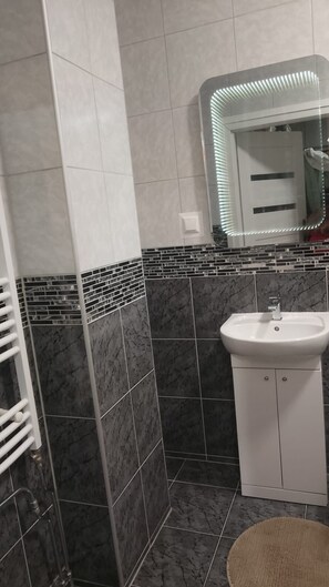 A bathroom with a white sink, a mirror with LED lights, and a tiled wall with a black and white pattern.