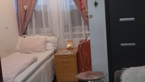 A bedroom with a bed, a small table, a wardrobe, and a window with sheer curtains. - Studio Sleeps 1 in Sundbyberg (Sundbyberg)
