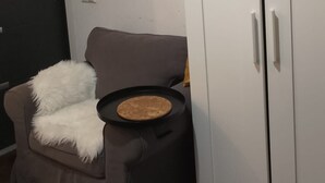 A room with a grey sofa, a small round table with a plate, a white wardrobe, and a dark door. - Studio Sleeps 1 in Sundbyberg (Sundbyberg)