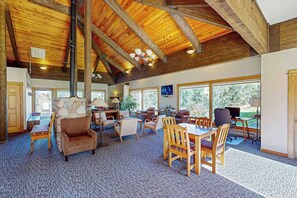 A spacious room with a high wooden ceiling, a fireplace, a dining area, and large windows offering a view of the outdoors. - Mountain-view condo with private balcony, grill, fireplace, on-site hot tub, gym (Steamboat Springs)