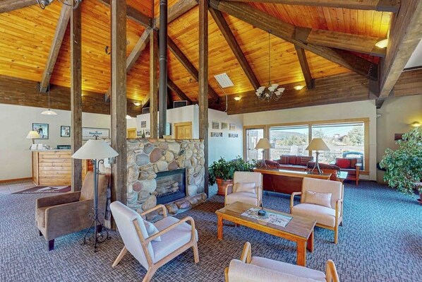 A spacious living area with a stone fireplace, wooden ceiling beams, and comfortable seating. - Mountain-view condo with private balcony, grill, fireplace, on-site hot tub, gym (Steamboat Springs)
