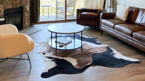 A living room with a stone fireplace, leather sofas, a round coffee table, and a large cowhide rug. - Ski Inn 211 - 2BR, 2BA ski-in/out condo with mountain views, fireplace, hot tub (Steamboat Springs)
