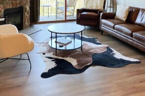 A living room with a stone fireplace, leather sofas, a round coffee table, and a large cowhide rug. - Mountain-view condo with private balcony, grill, fireplace, on-site hot tub, gym (Steamboat Springs)