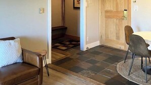 A room with a brown leather sofa, a round table with chairs, a wooden door, and a checkered floor pattern. - Ski Inn 211 - 2BR, 2BA ski-in/out condo with mountain views, fireplace, hot tub (Steamboat Springs)