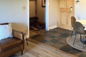 A room with a brown leather sofa, a round table with chairs, a wooden door, and a checkered floor pattern. - Mountain-view condo with private balcony, grill, fireplace, on-site hot tub, gym (Steamboat Springs)