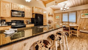 Eine Küche mit Holzausbau, einem schwarzen Kühlschrank, einer Mikrowelle, einem Herd, einer Spüle und einer Bar mit Hockern.