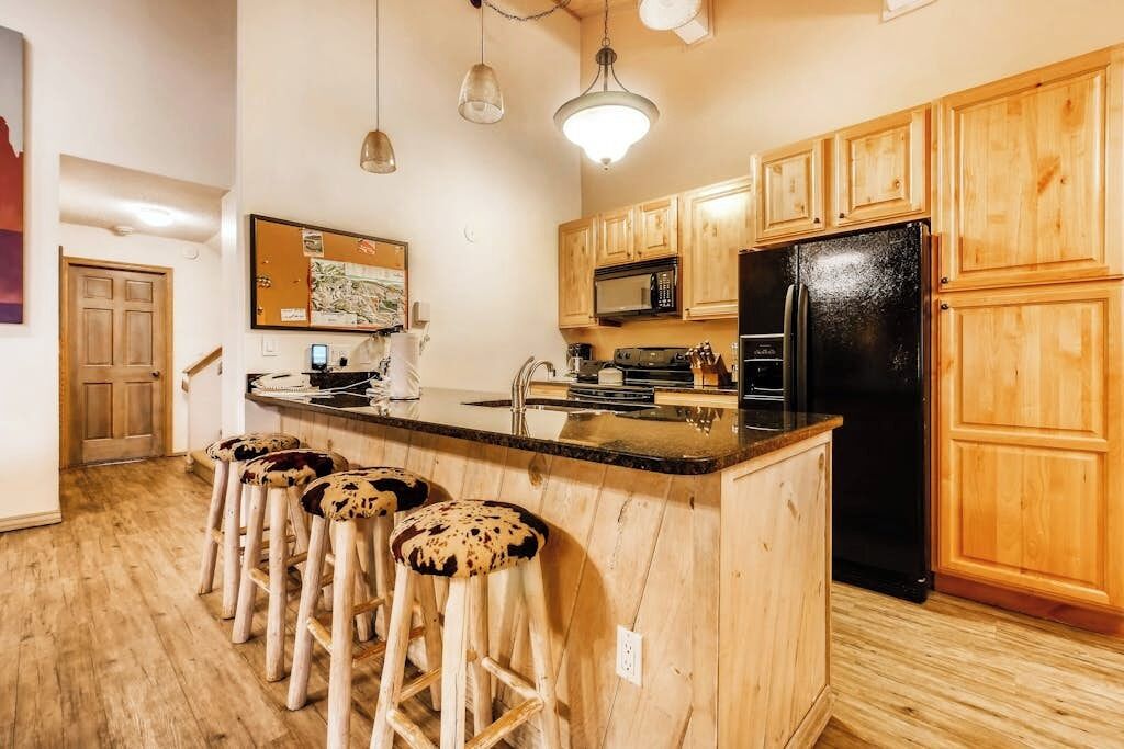 A kitchen with wooden cabinets, a black refrigerator, a microwave, and a bar stool area.