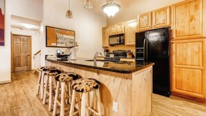 Eine Küche mit Holzausstattung, einem schwarzen Kühlschrank, einer Mikrowelle und einer Bar mit Barhocker.