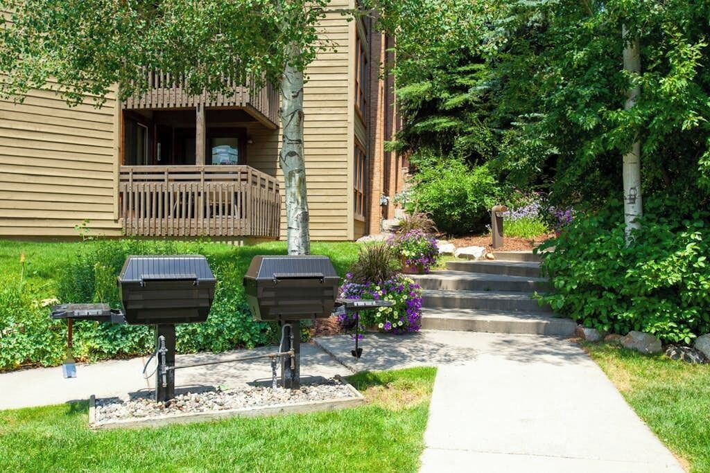 A building with a wooden balcony, outdoor grills, and a pathway leading to the entrance.