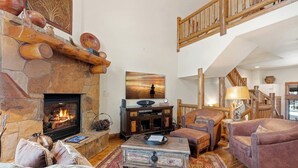 Una sala de estar acogedora con chimenea de piedra, una escalera de madera y un área de descanso cómoda.