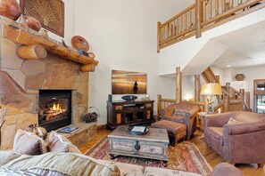 Ein gemütliches Wohnzimmer mit Kamin aus Stein, einer Holztreppe und einer komfortablen Sitzecke.