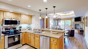 A modern kitchen with wooden cabinets, stainless steel appliances, a central island, and pendant lighting. - Canyon Creek B306 - Spacious condo with pool, hot tub, gym & easy walk to lifts (Steamboat Springs)