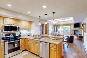A modern kitchen with wooden cabinets, stainless steel appliances, a central island, and pendant lighting. - Spacious condo with pool, hot tub, gym & easy walk to lifts (Steamboat Springs)