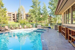 A swimming pool with lounge chairs and a bar area, surrounded by trees and buildings. - Spacious condo with pool, hot tub, gym & easy walk to lifts (Steamboat Springs)