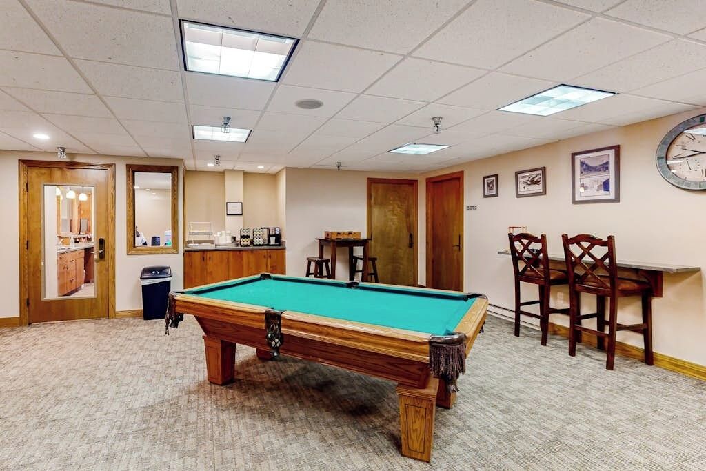 A pool table in a room with a carpeted floor, wooden furniture, and framed pictures on the walls.
