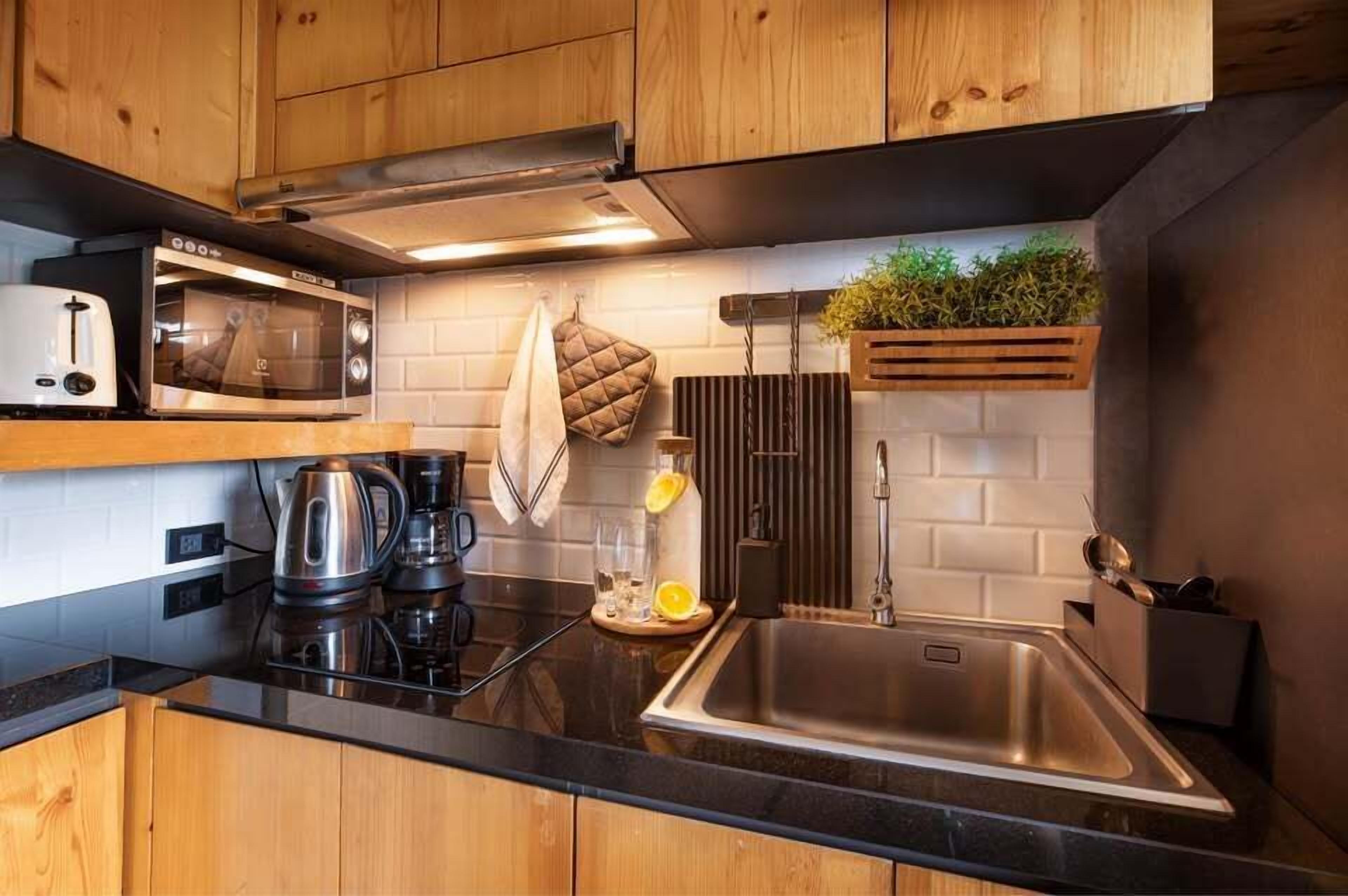 A modern kitchen with wooden cabinets, a microwave, a kettle, a sink, and a plant on the wall.