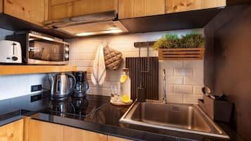 A modern kitchen with wooden cabinets, a microwave, a kettle, a sink, and a plant on the wall.