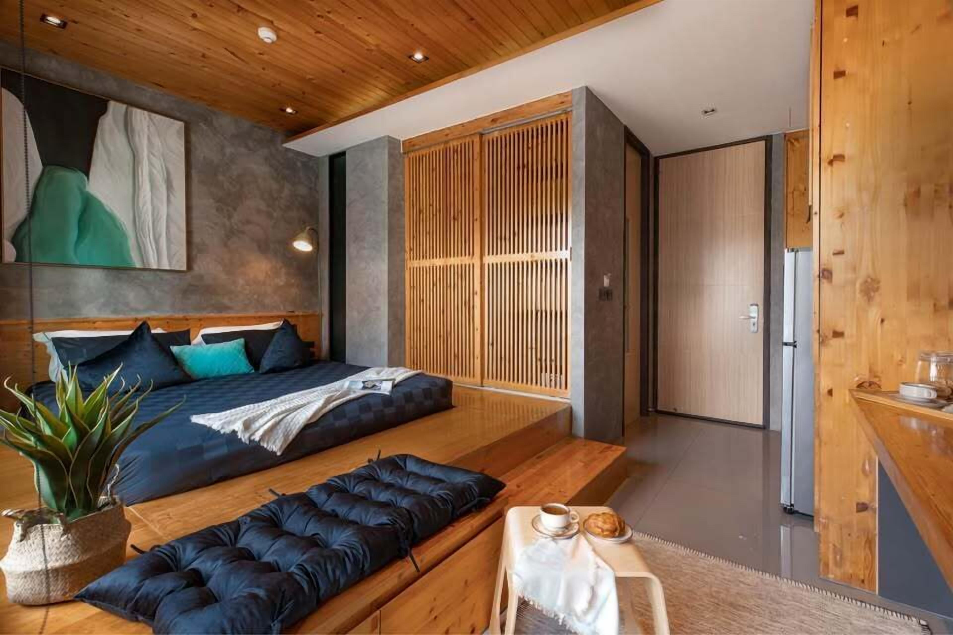 A modern bedroom with a bed, a seating area, a small table with a cup and pastry, and a wooden wardrobe.