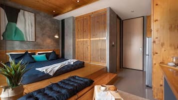 A modern bedroom with a bed, a seating area, a small table with a cup and pastry, and a wooden wardrobe.