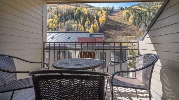 Een balkon met rieten stoelen en een kleine tafel, met uitzicht op een bebost heuvellandschap.