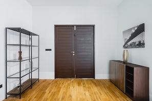 Ein Flur mit Holzboden, einer dunkelbraunen Tür, einem Metallregal und einem Schrank mit einer Vase.