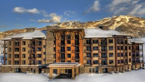 A multi-story hotel with balconies, a covered outdoor seating area, and a mountainous backdrop. - Convenient Home Close to Steamboat Ski Resort, Hiking Trails, Restaurants & More (Steamboat Springs)
