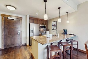 Eine Küche mit Granit Arbeitsplatte, Holzstühlen, einem Kühlschrank, einer Mikrowelle und Pendelleuchten.