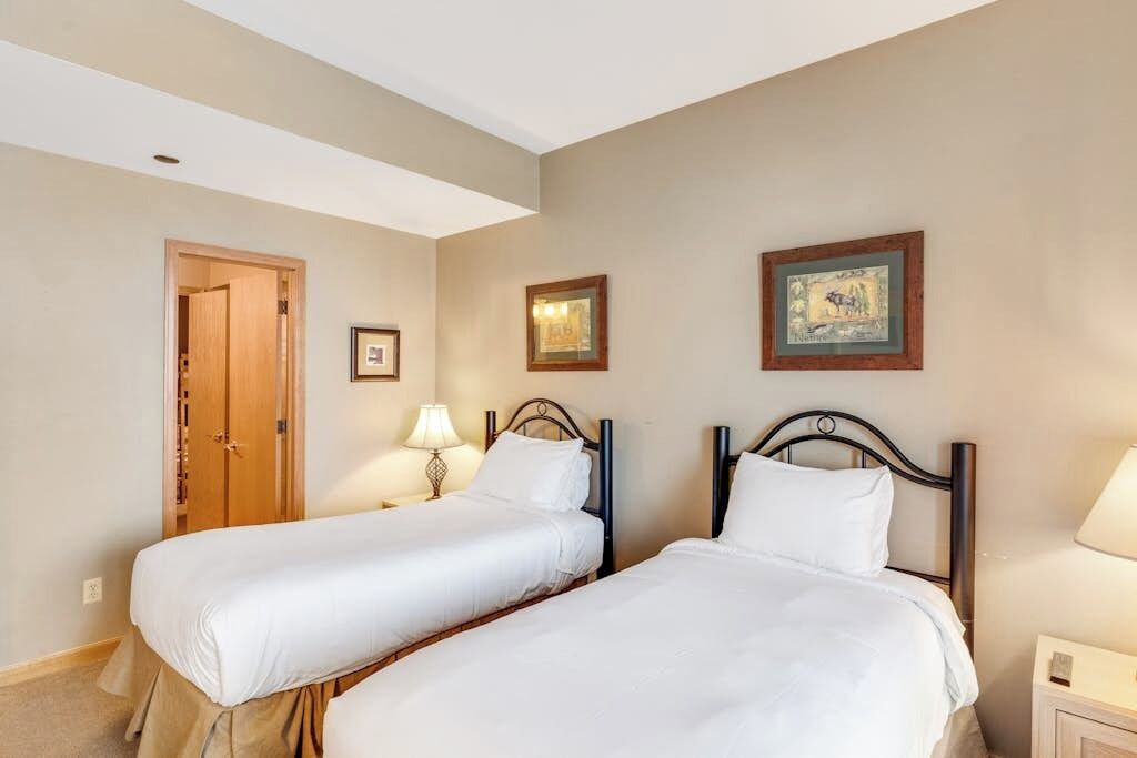 A hotel room with two beds, a wooden door, and framed pictures on the wall.