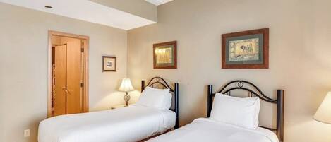A hotel room with two beds, a wooden door, and framed pictures on the wall.